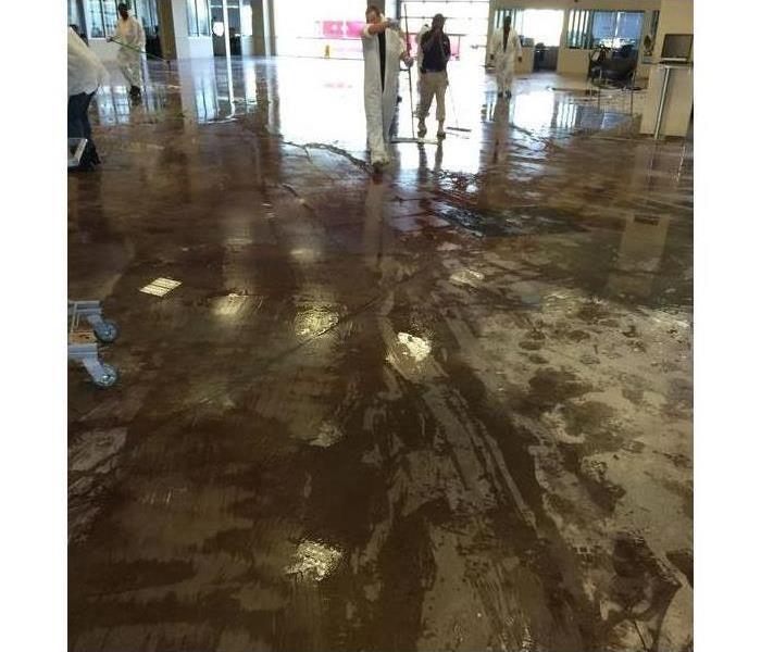 Wet floor of a commercial building, workers cleaning water from a building and wearing protective gear